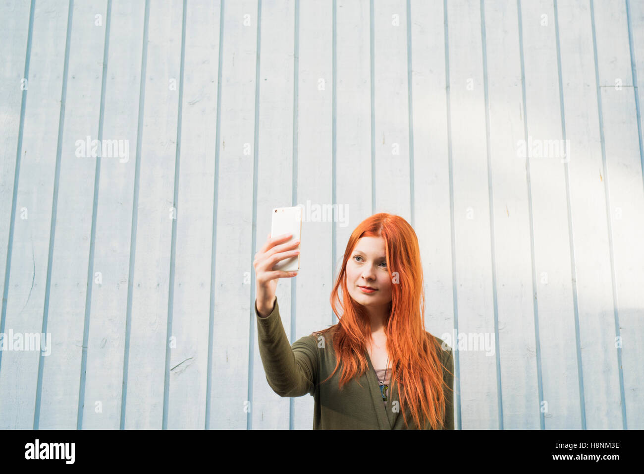 Redhaired donna prendendo selfie contro il muro bianco Foto Stock