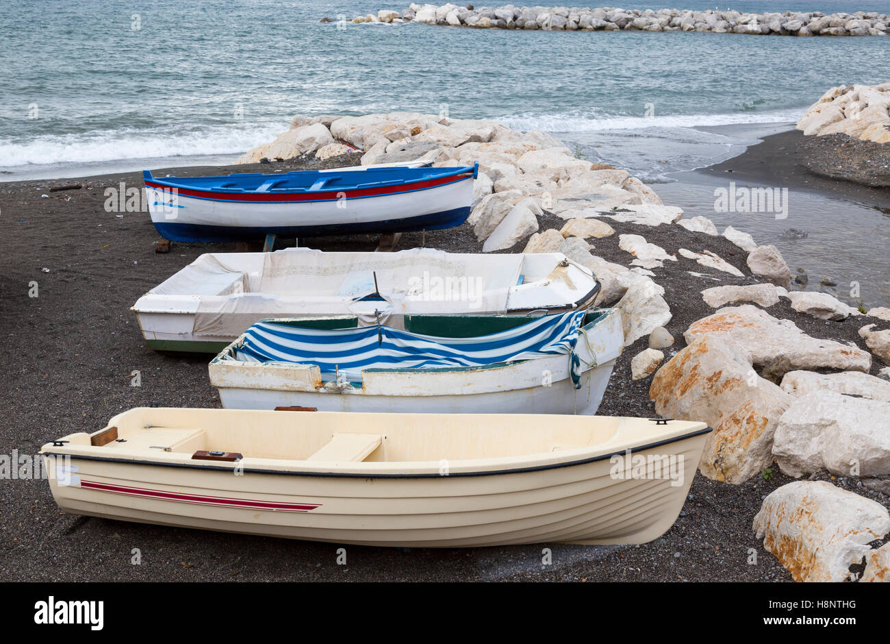 Barche di pescatori sulla spiaggia, lungo la barriera di roccia, oceano oltre Foto Stock