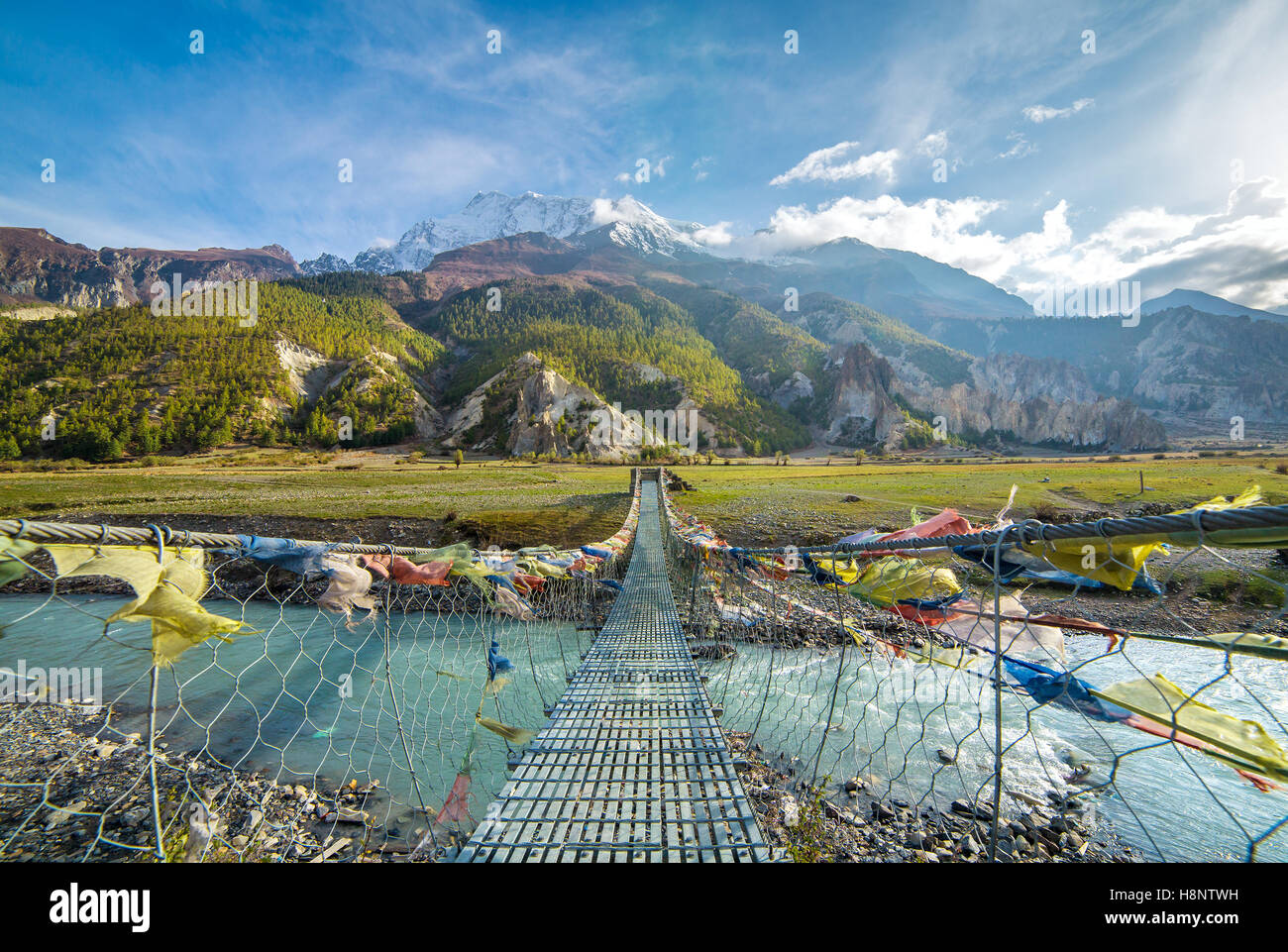 Ponte di sospensione con la preghiera buddista bandiere sul circuito di Annapurna trek in Nepal. Shangri-la terra Foto Stock