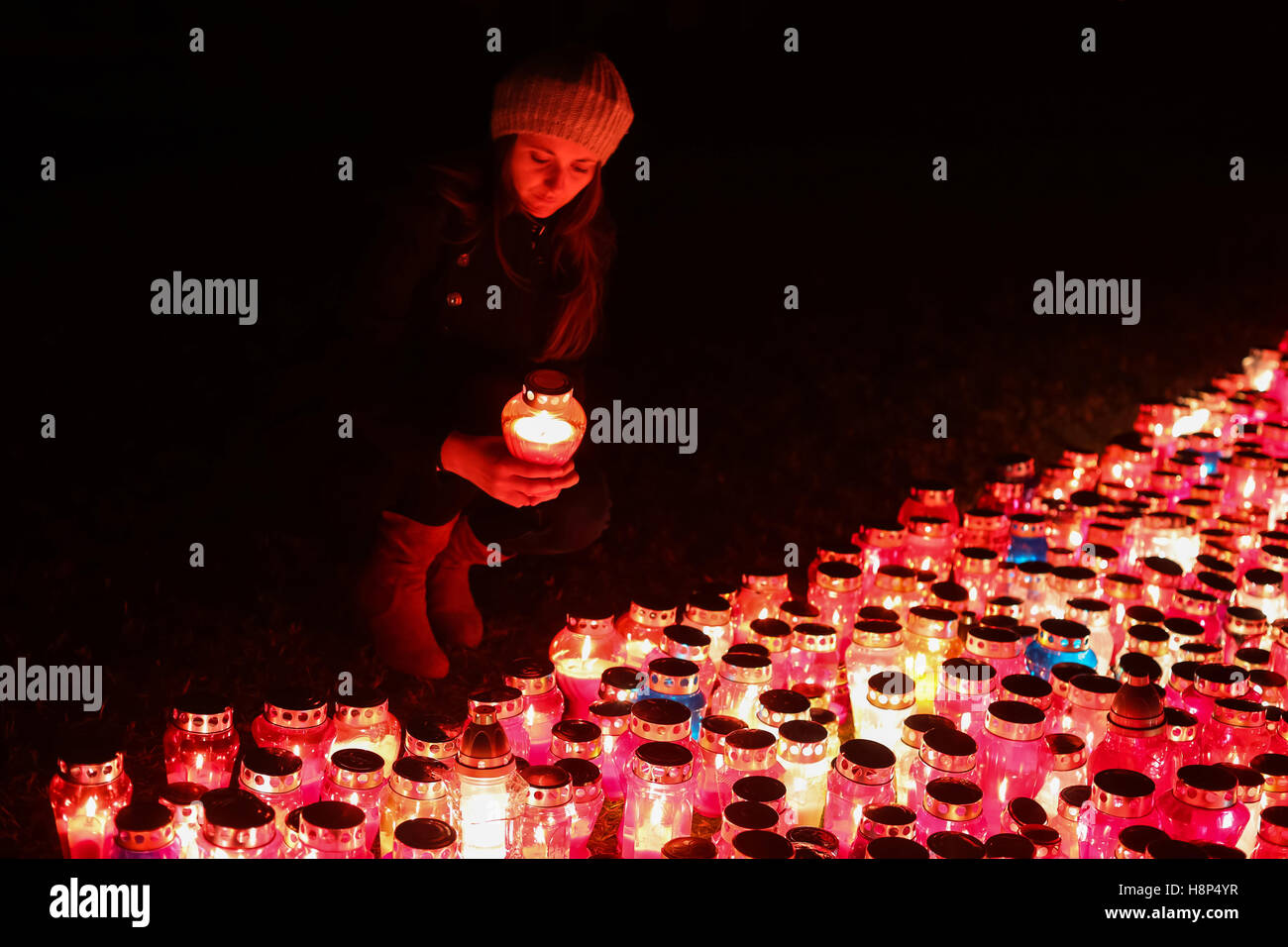 Una vista notturna di una donna tenendo un lampion davanti a un folto gruppo di bruciare lampions sul pavimento al cimitero in Croazia. Foto Stock