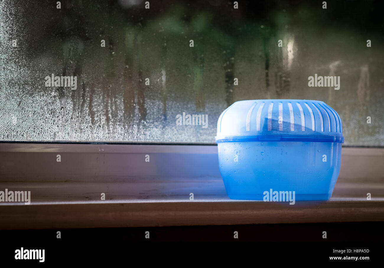 Una plastica assorbitore di umidità trappola di acqua su un davanzale con la formazione di condensa sulla finestra dietro Foto Stock