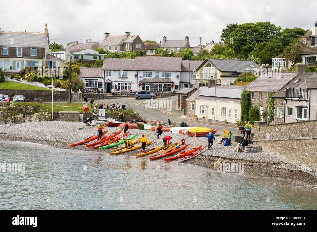 Canoe e canoisti sulla spiaggia di ciottoli di Moelfre Bay, nel villaggio di Moelfre, Anglesey, Galles Foto Stock