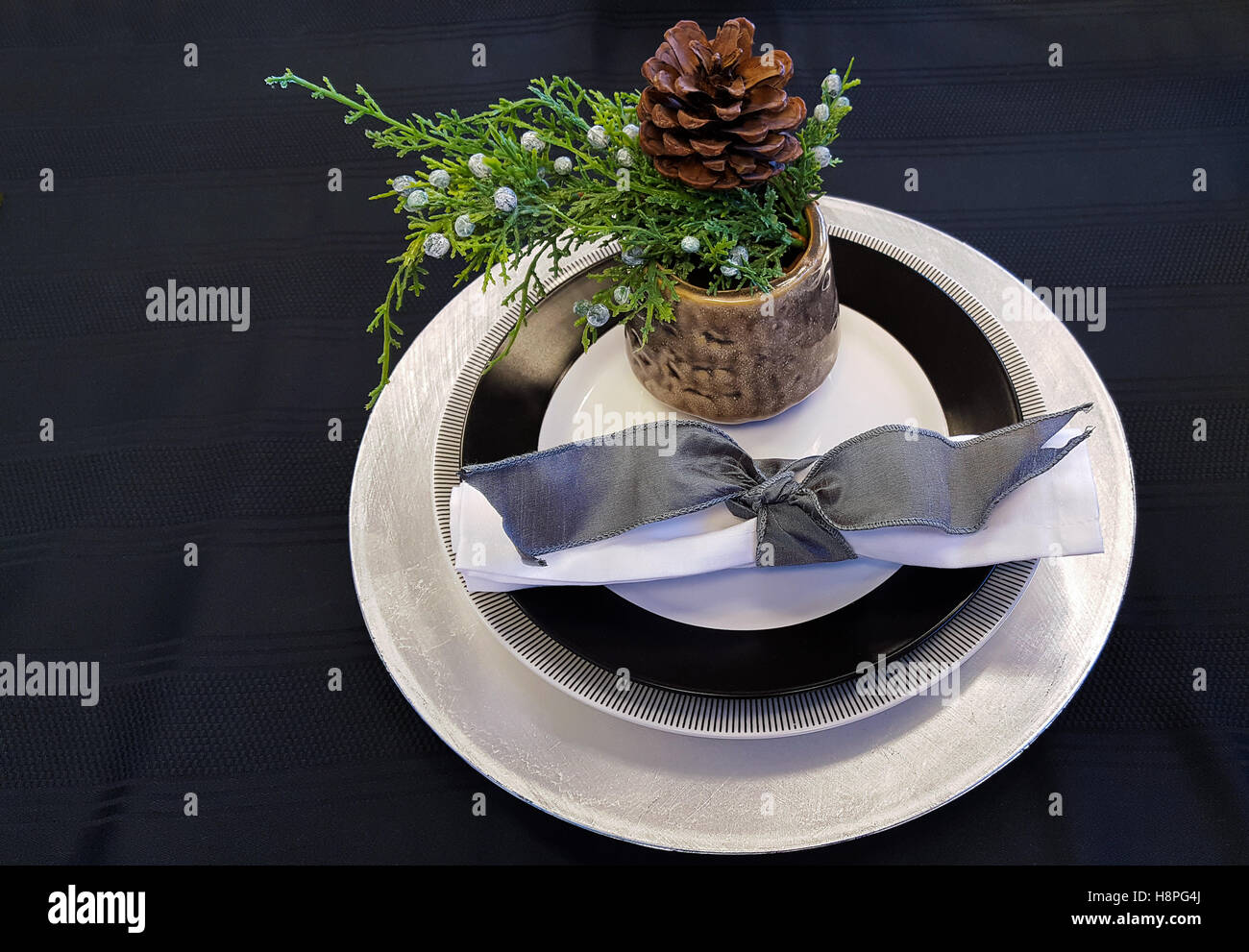 Evergreen in coppa con piastra di Natale impostazione sulla tovaglia nero Foto Stock