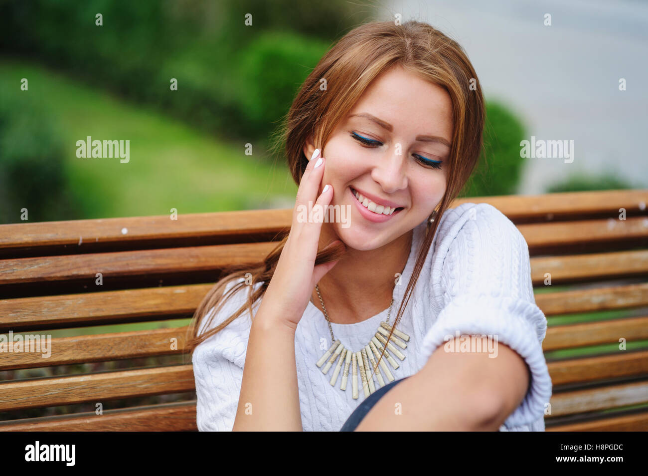 Felice giovane donna seduta su una panchina nel parco Foto Stock