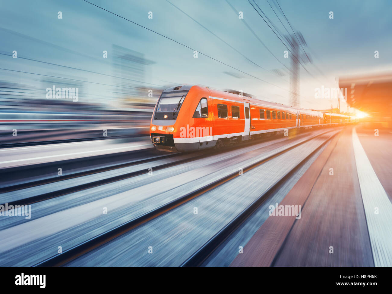 Moderna e alta velocità passeggeri rosso treni pendolari in movimento con la piattaforma ferroviaria al tramonto. Stazione ferroviaria. Ferrovia Foto Stock