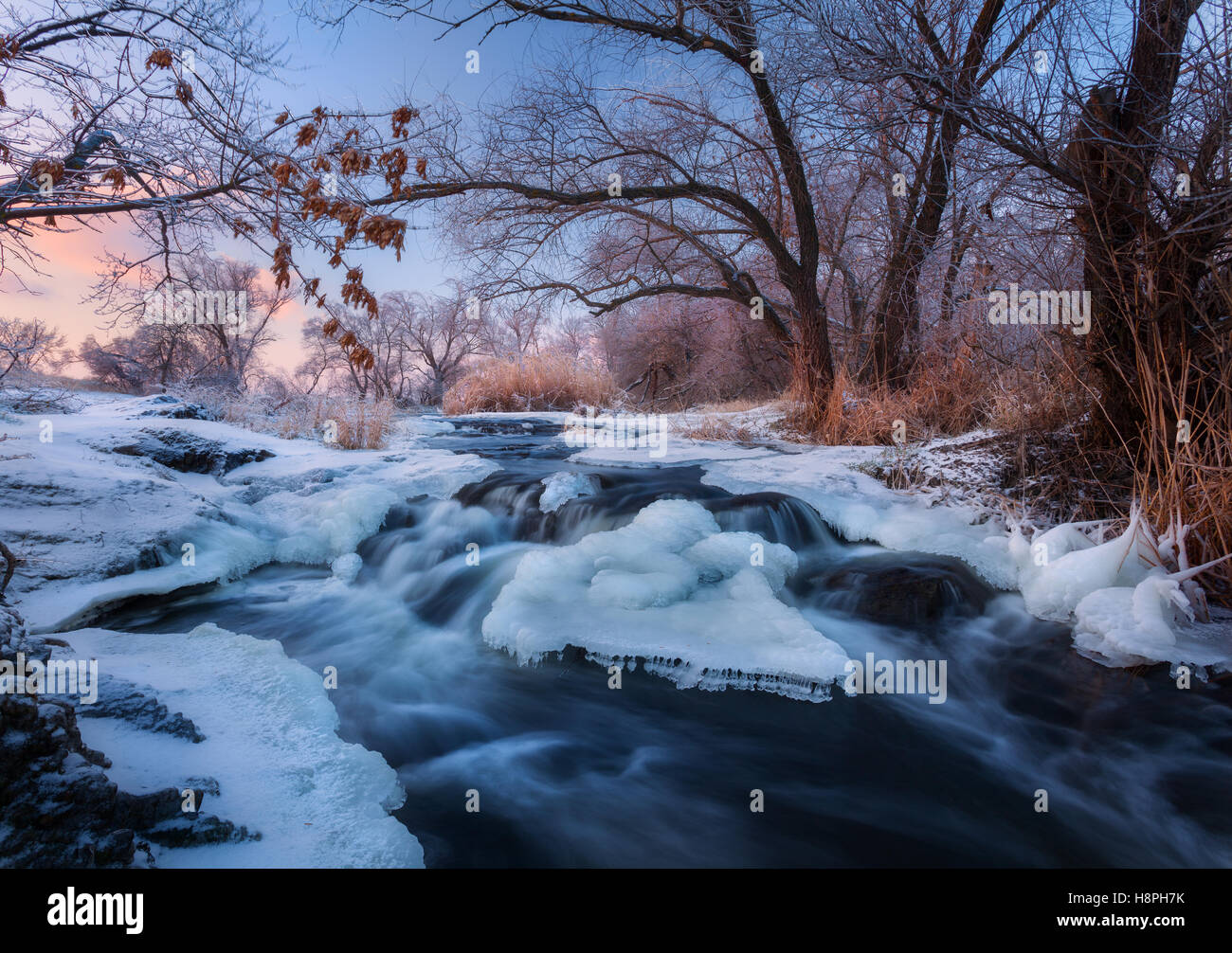 Paesaggio invernale con alberi innevati, bellissimo fiume congelato e cespugli al tramonto. Foresta d'inverno. Vista con inverno alberi, giallo ri Foto Stock