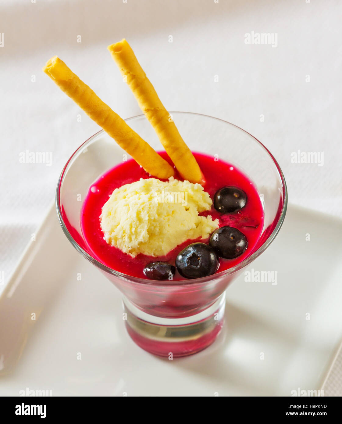 Un dessert di succo di mirtillo e rabboccato con una pallina di gelato alla vaniglia e guarnito con mirtilli e wafer Foto Stock