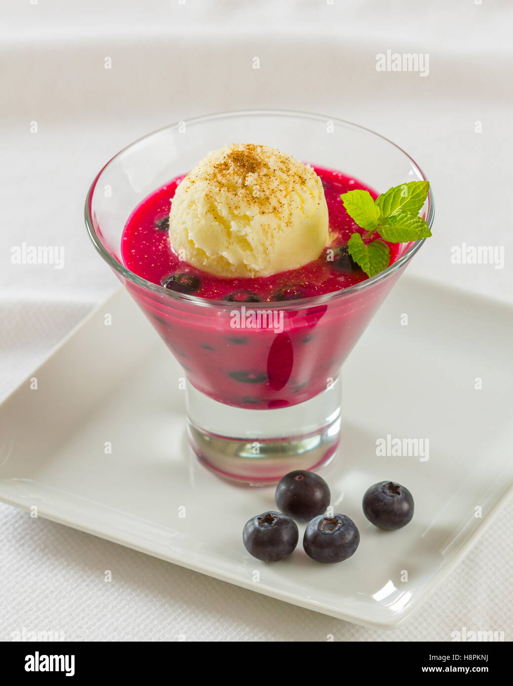 Un dessert di succo di mirtillo e rabboccato con una pallina di gelato alla vaniglia e guarnito con mirtilli Foto Stock