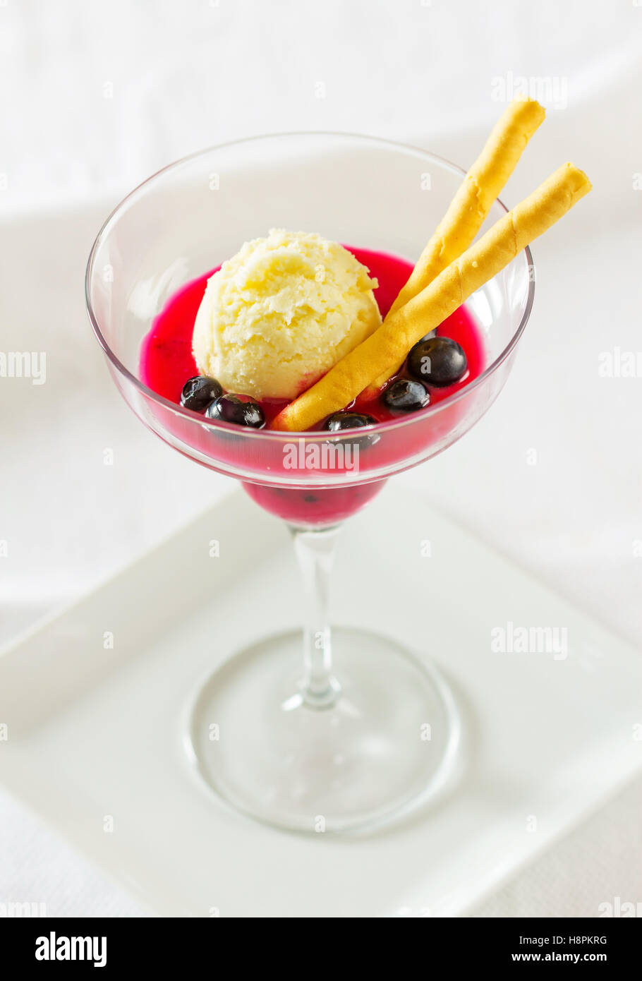 Un dessert di succo di mirtillo e rabboccato con una pallina di gelato alla vaniglia e guarnito con mirtilli e wafer Foto Stock