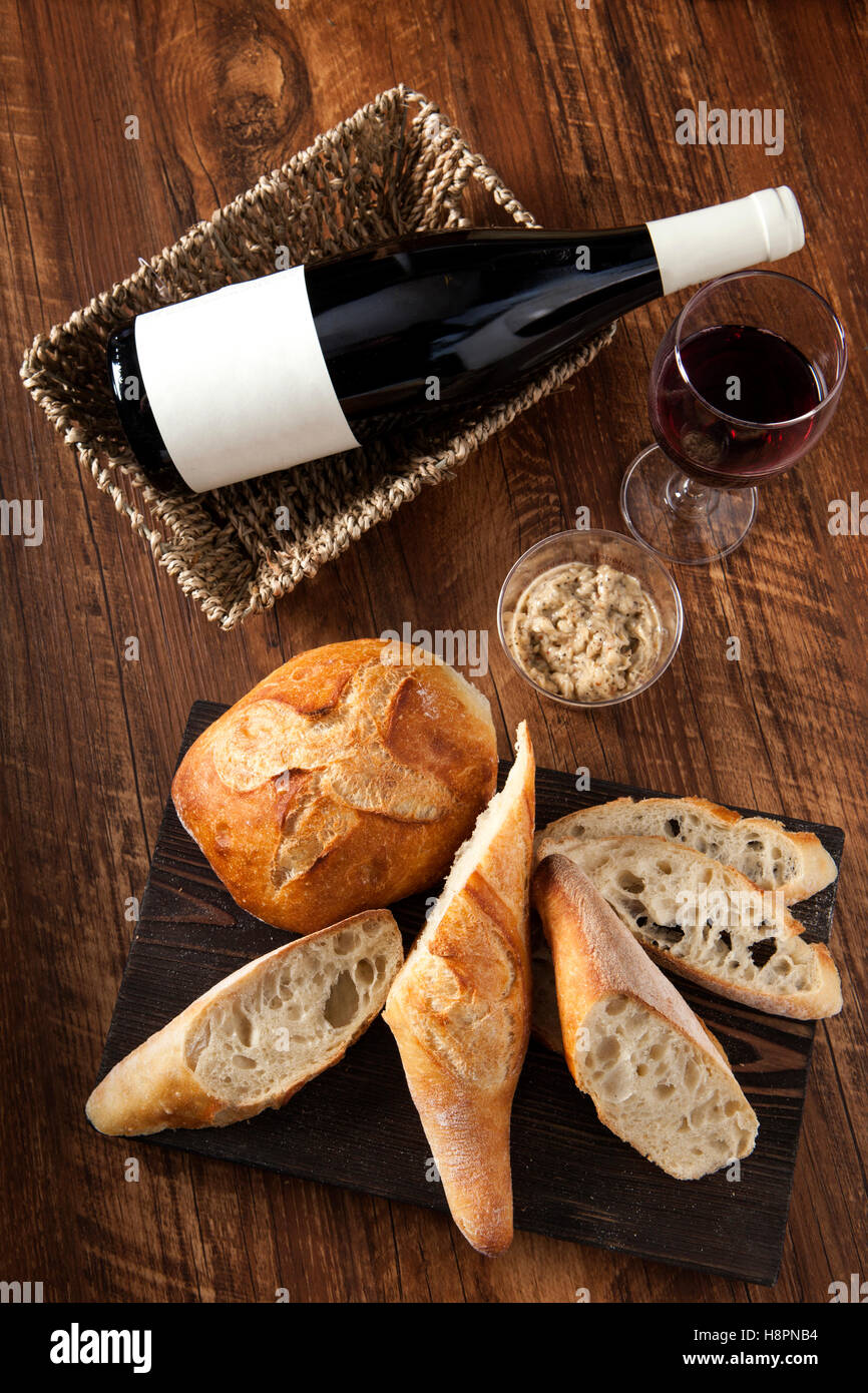 Baguette e la pagnotta di pane con vino rosso sul tavolo di legno Foto Stock