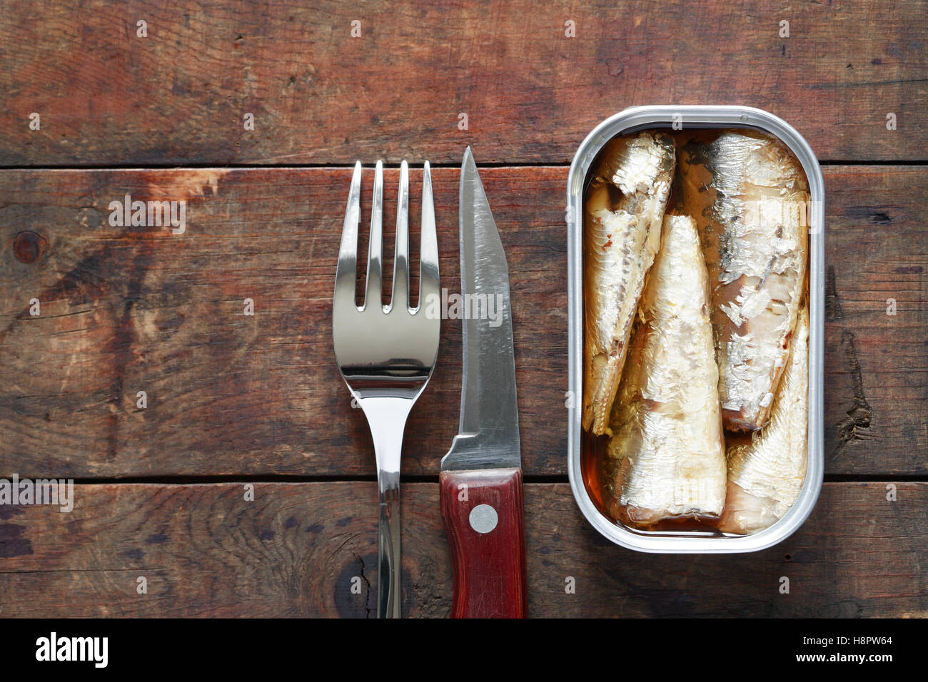 Aprire il pesce in scatola vicino a forchetta e coltello sullo sfondo di legno con spazio libero Foto Stock