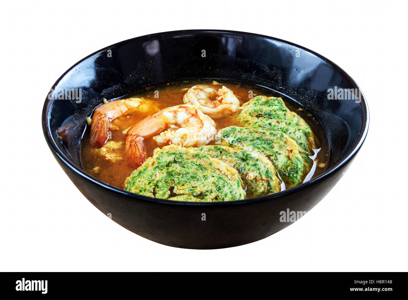 Calda e acida curry Zuppa di gamberetti e di acacia pennata frittata. In piatto nero su sfondo bianco. Gli oggetti con i tracciati di ritaglio Foto Stock