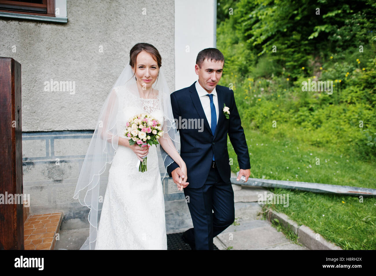 Coppie in viaggio di nozze a piedi giù per le scale per chiesa tenendo le mani Foto Stock
