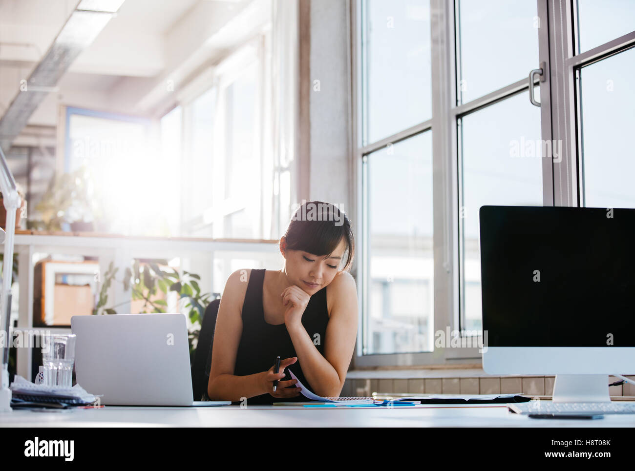 Colpo di bella giovane donna seduta alla sua scrivania passando attraverso alcuni documenti. Asian imprenditrice lavorando nei moderni offic Foto Stock