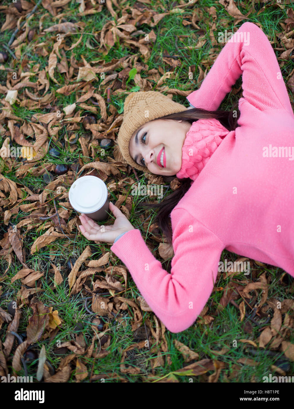 Ragazza distesa su foglie di autunno con caffè guardando lontano Foto Stock
