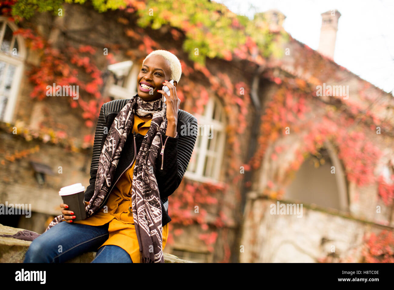 Moderno e giovane africano donna americana in posa con caffè di andare e il telefono cellulare all'aperto Foto Stock