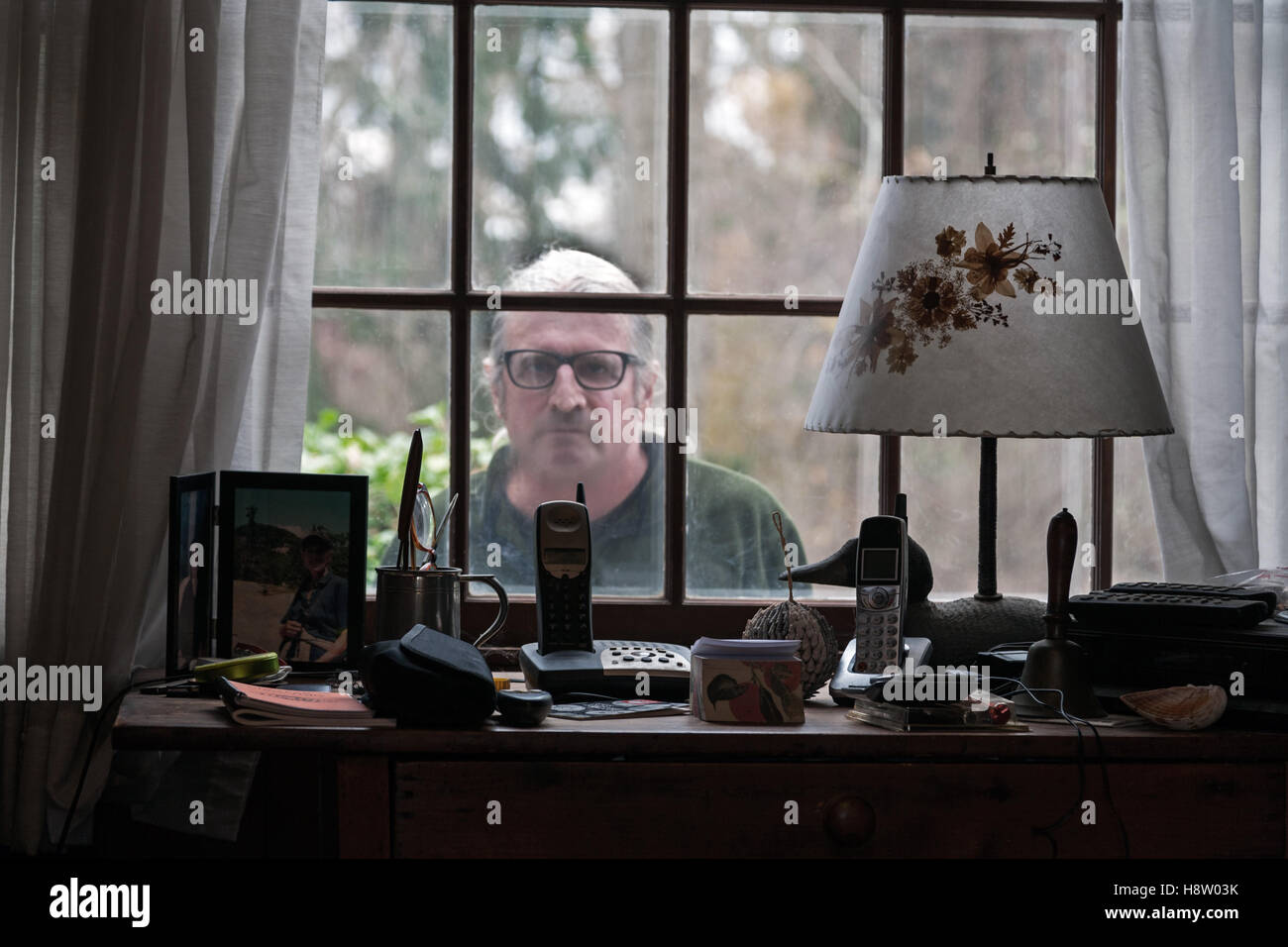 Mid-Adult uomo del peering attraverso la finestra di casa Foto Stock