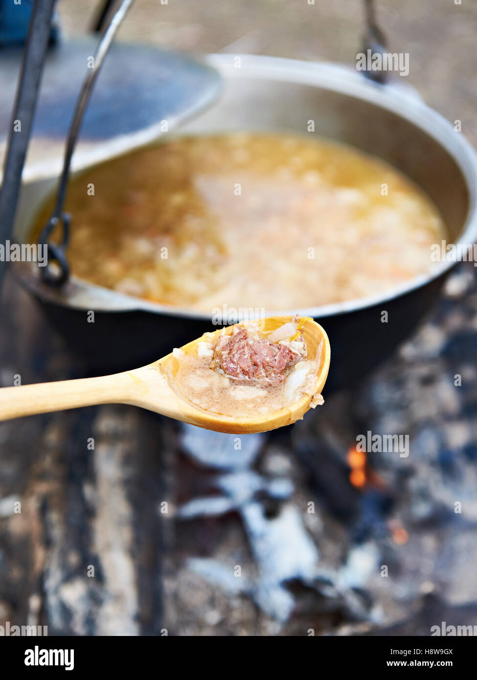 Il cucchiaio di legno con il cibo oltre il fuoco in una escursione Foto Stock