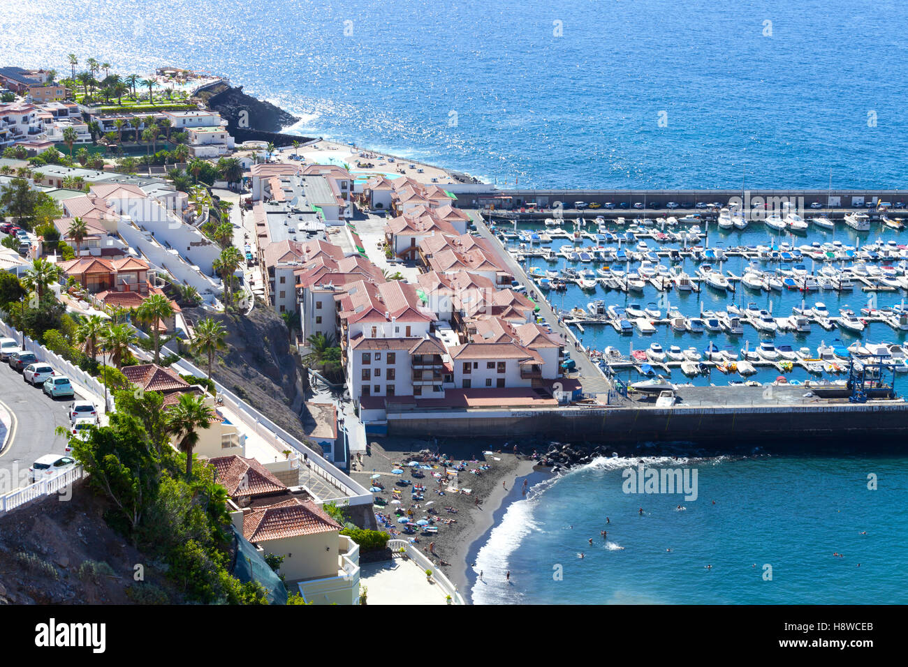 Vista aerea della città costiera di Los Gigantes a Tenerife, con una piccola barca porta , di colore scuro sabbia spiaggia , ville in collina Foto Stock