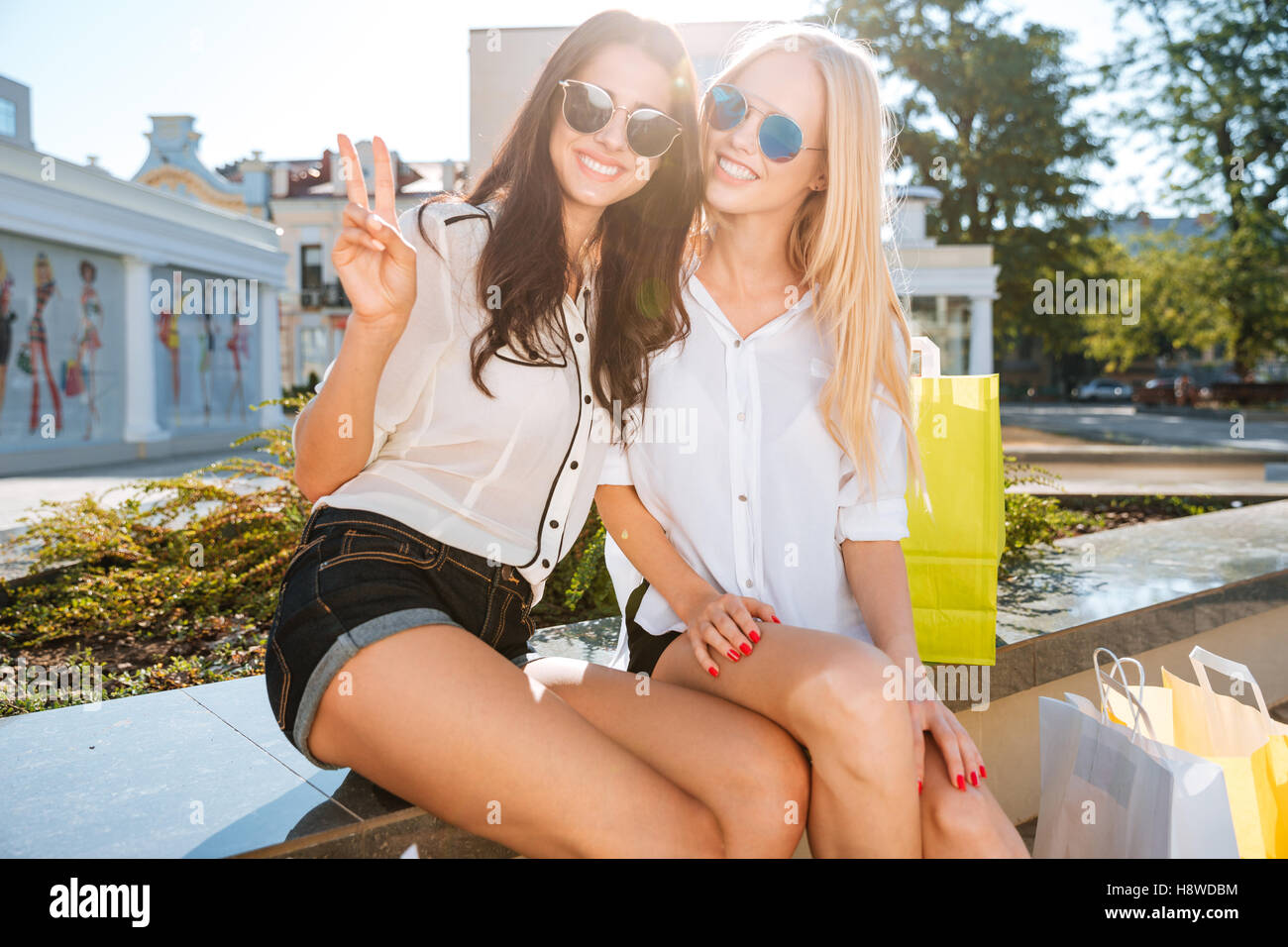 Due donne in appoggio su un banco di lavoro insieme dopo lo shopping e mostra il gesto di vittoria Foto Stock