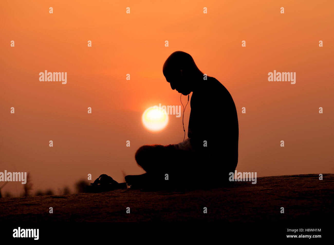 Maschio adulto nella foto stagliano contro un ambiente Sun, con auricolare e fili mostra, ascolto di musica e la meditazione Foto Stock