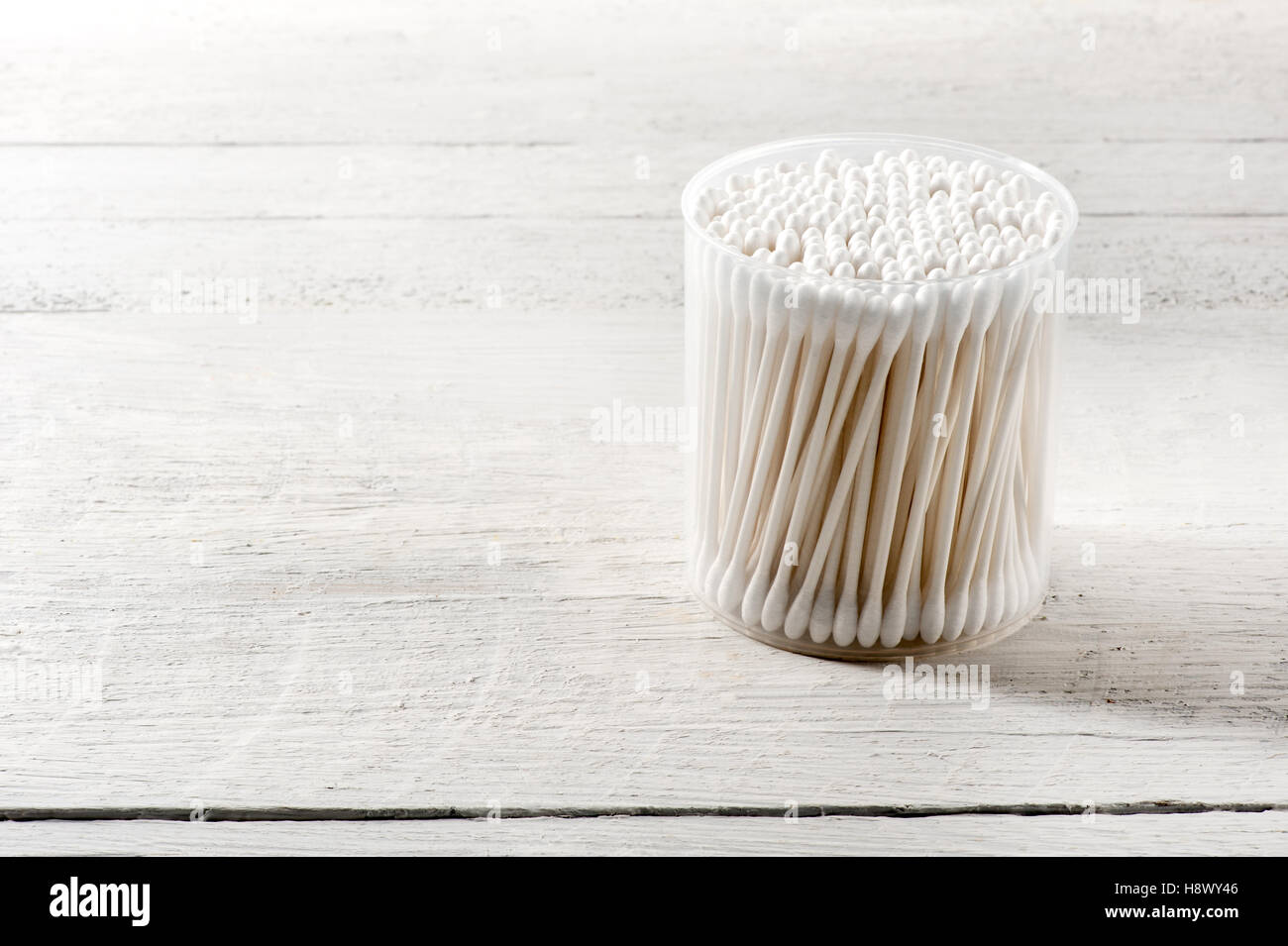 Contenitore di plastica cilindrico pulito di cotone bianco gemme in una cura di salute e igiene del concetto su un bianco tavola di legno Foto Stock