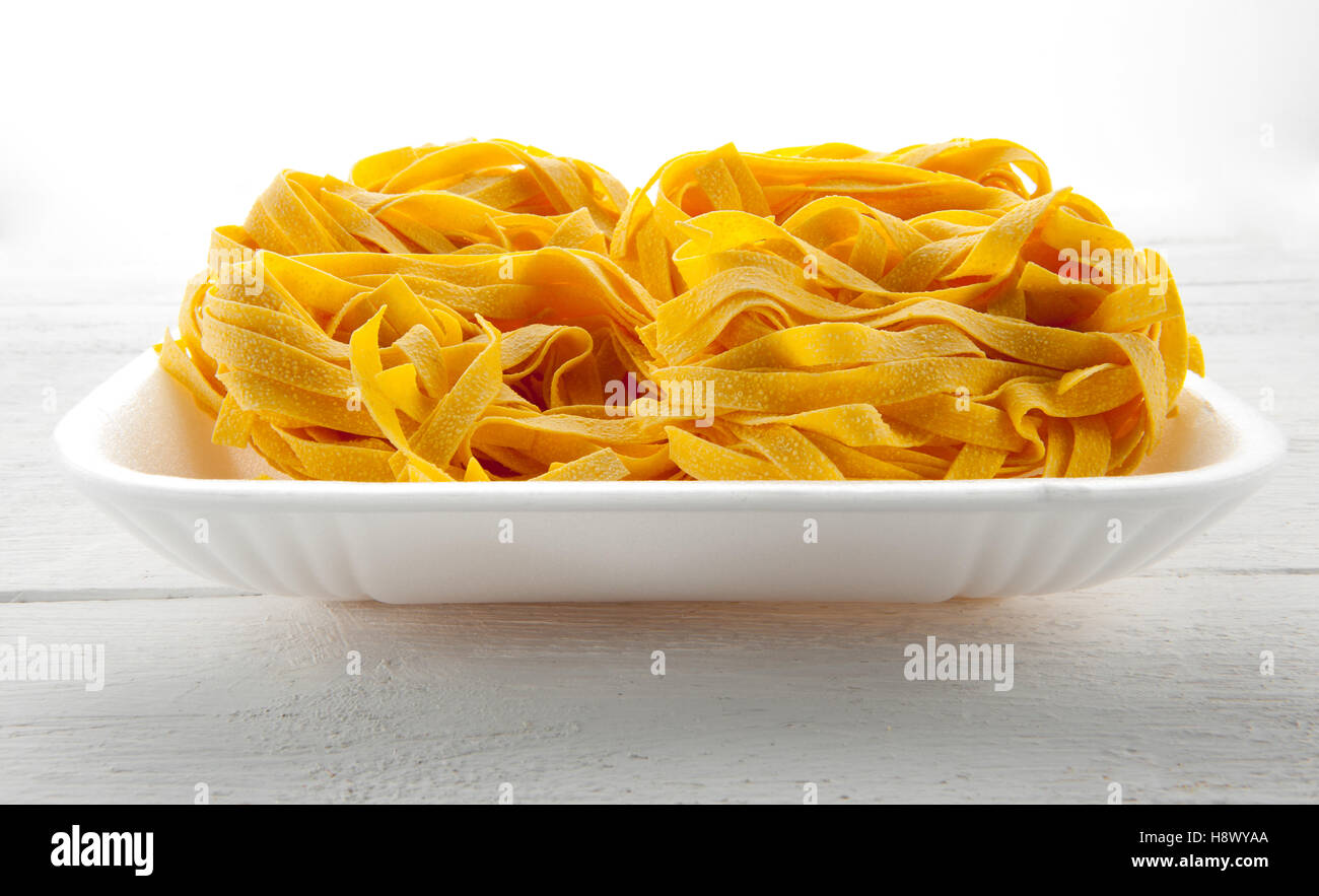 Tumulo di tagliatelle su un vassoio bianco pronto per l'uso come ingrediente in cucina tradizionale italiana Foto Stock