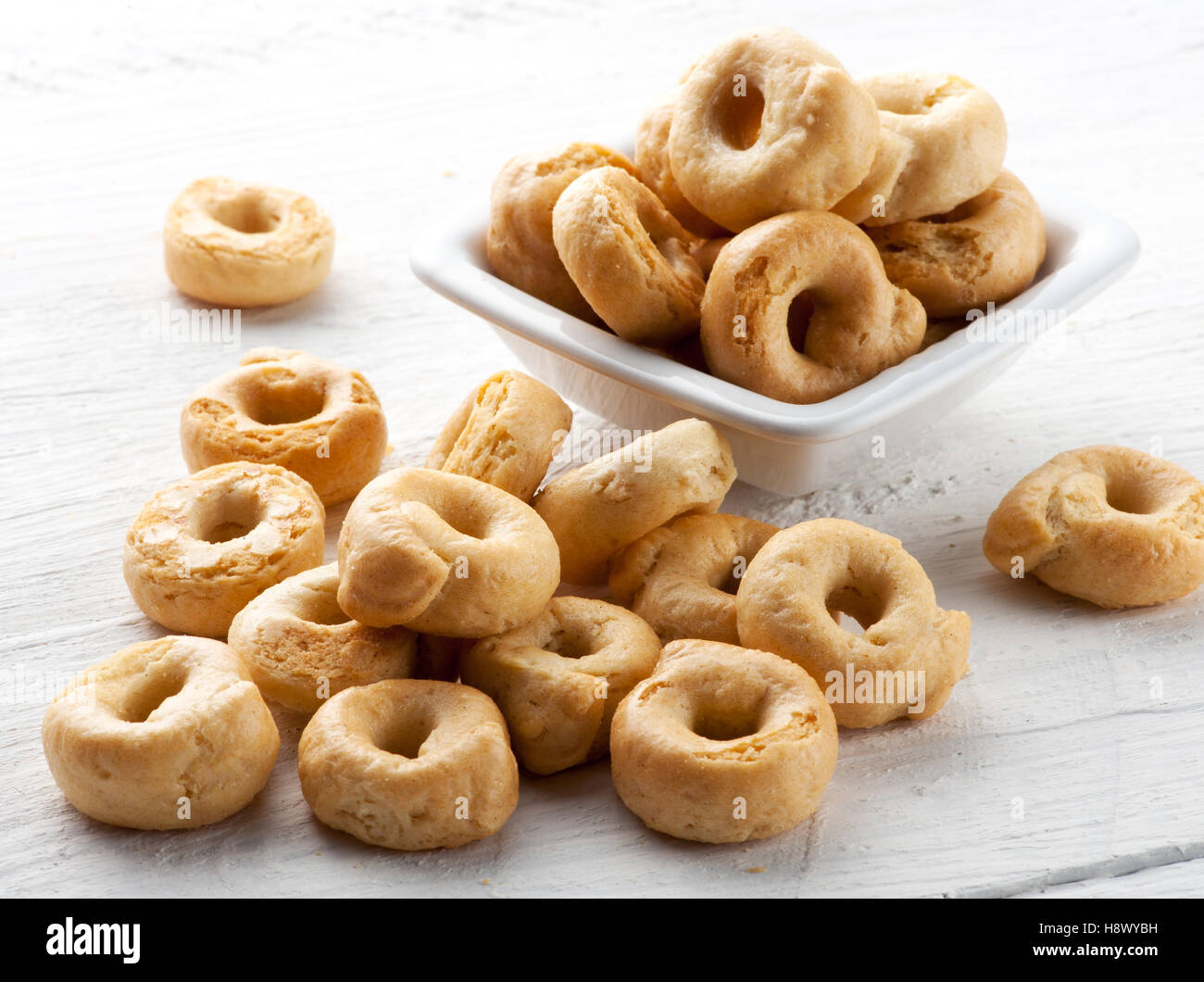 Italian taralli cracker per un dito di deliziosi snack servito in una piccola ciotola versarsi in una pila sul bianco di un pannello di legno Foto Stock