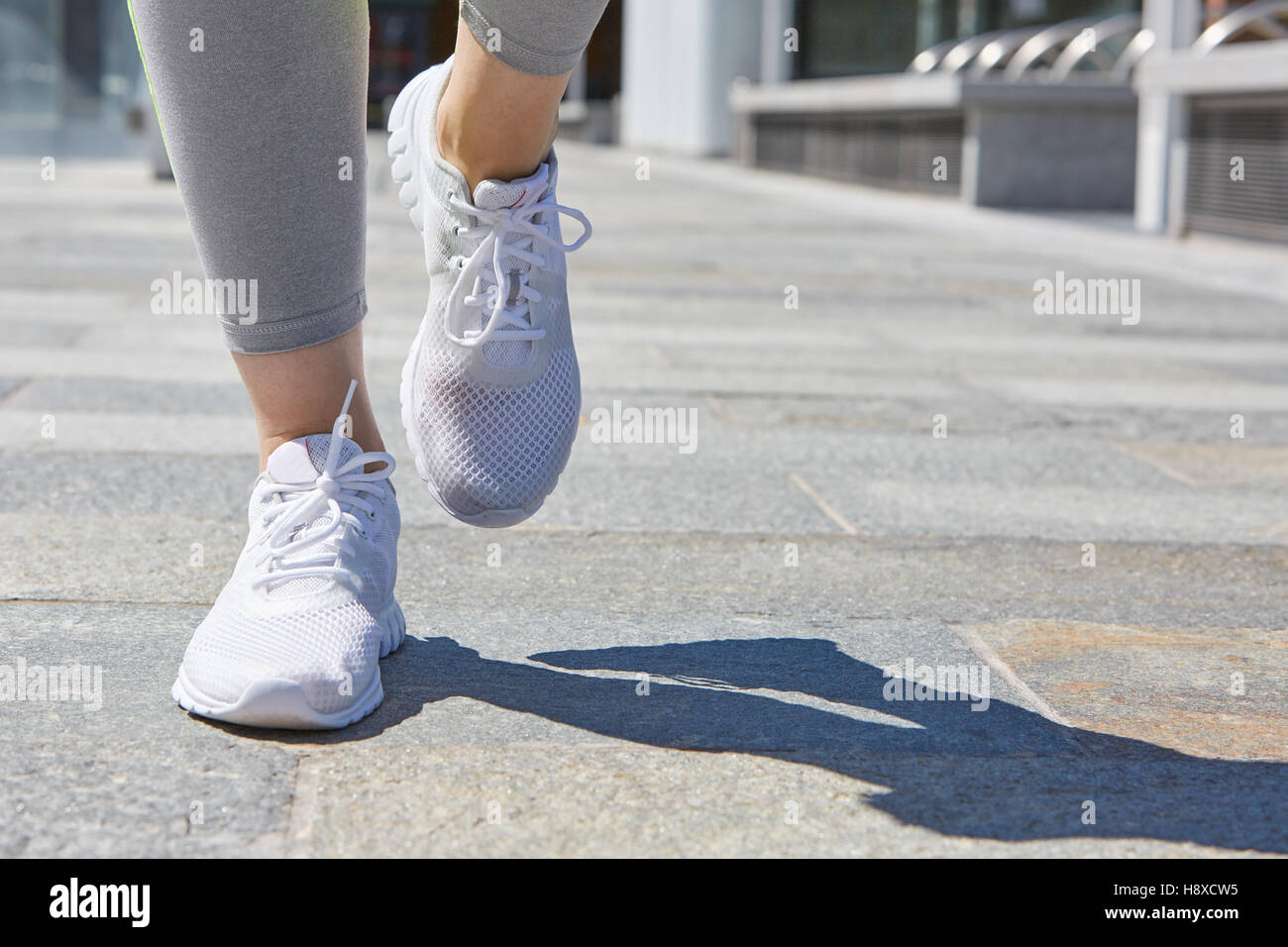 Donna in corsa con le scarpe di colore bianco per esterno in città in una giornata di sole Foto Stock