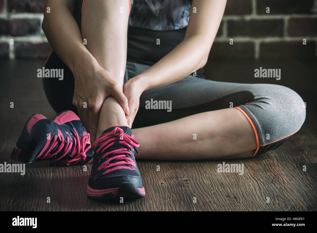 La sua caviglia feriti in palestra fitness training esercizio, uno stile di vita sano concetto, in interni con pavimento in legno e parete di mattoni sfondo Foto Stock