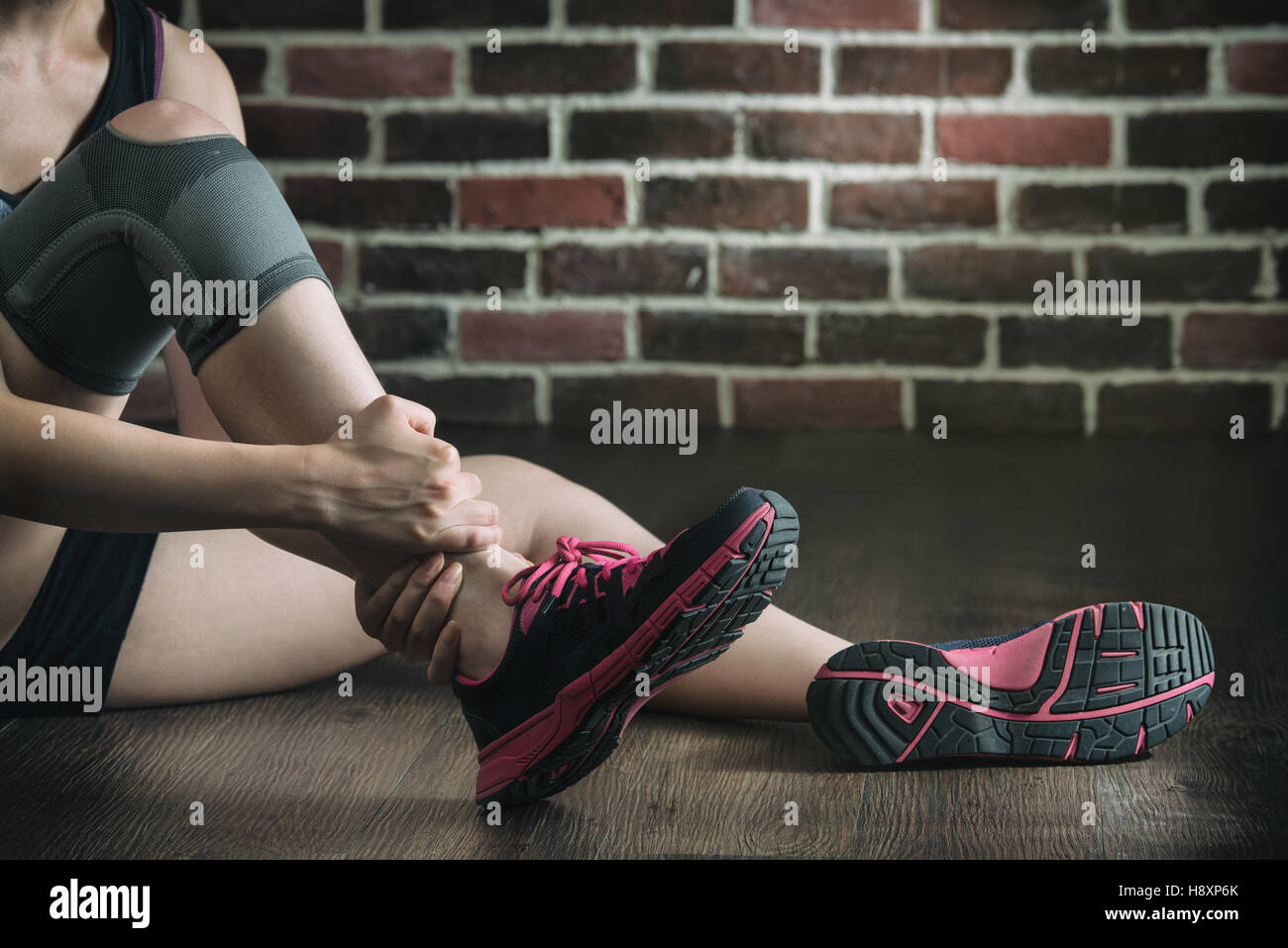 La sua caviglia feriti in palestra fitness training esercizio, uno stile di vita sano concetto, in interni con pavimento in legno e parete di mattoni sfondo Foto Stock