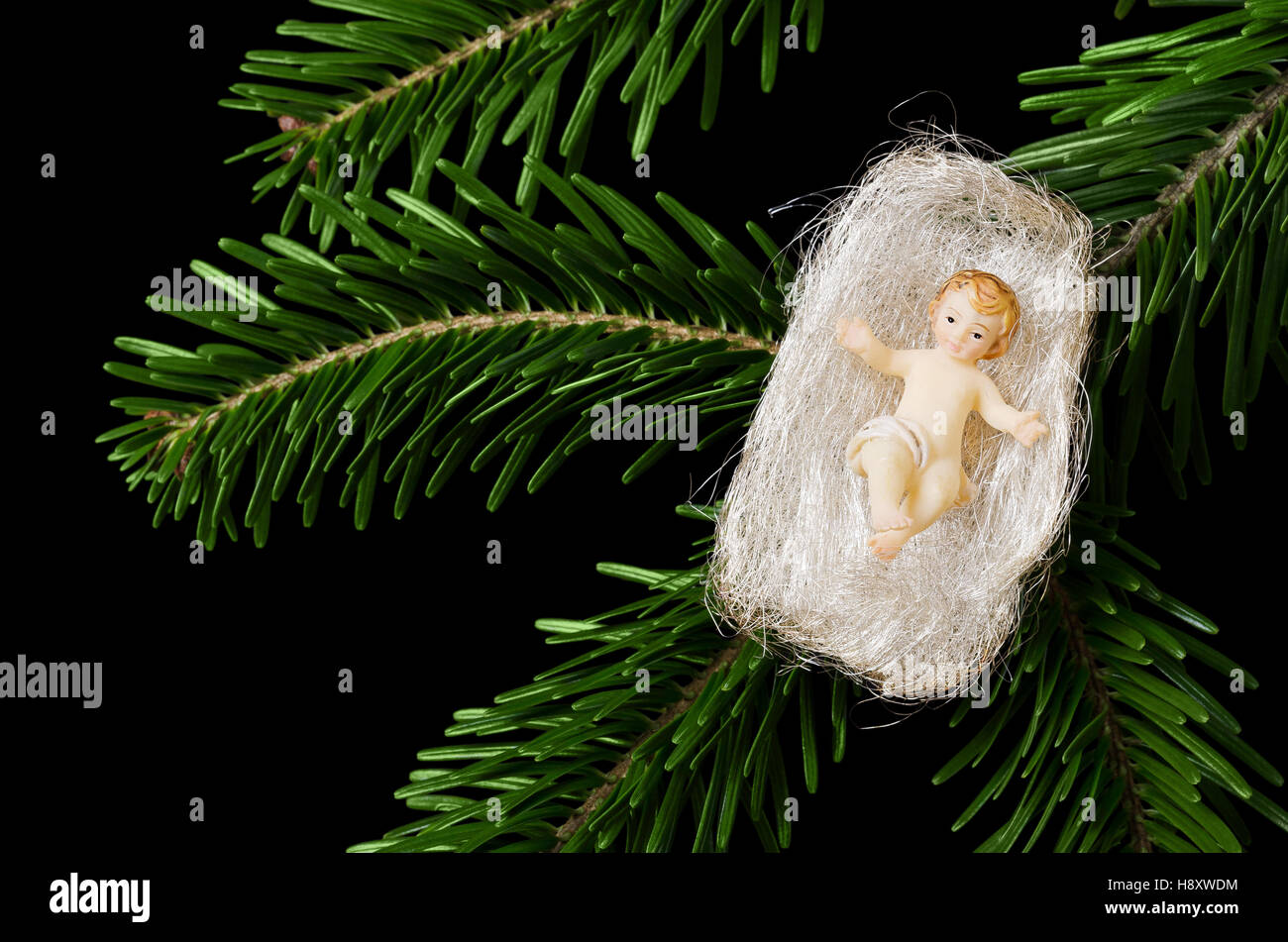 Cristo bambino statuetta in Angel Hair su un ramo di abete su sfondo nero. Artigianali a Gesù Bambino Decorazione per albero di Natale. Foto Stock