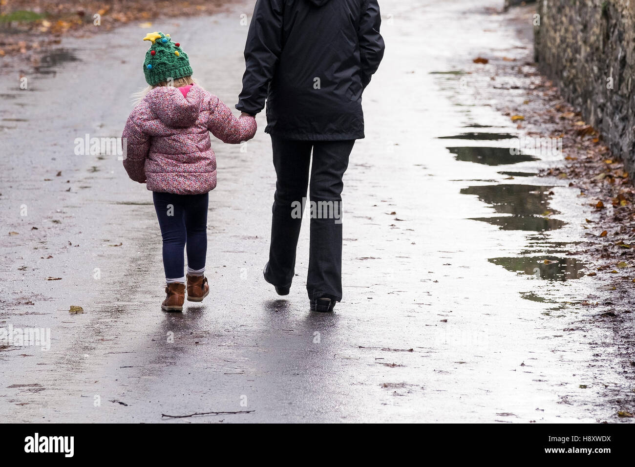 Un bambino e un adulto camminando mano nella mano con una strada in discesa. Foto Stock