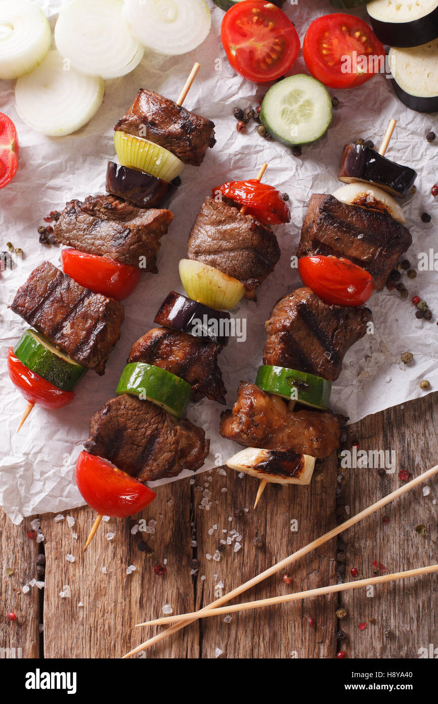 Shish kebab su spiedini con verdure vicino sul tavolo. vista verticale da sopra Foto Stock