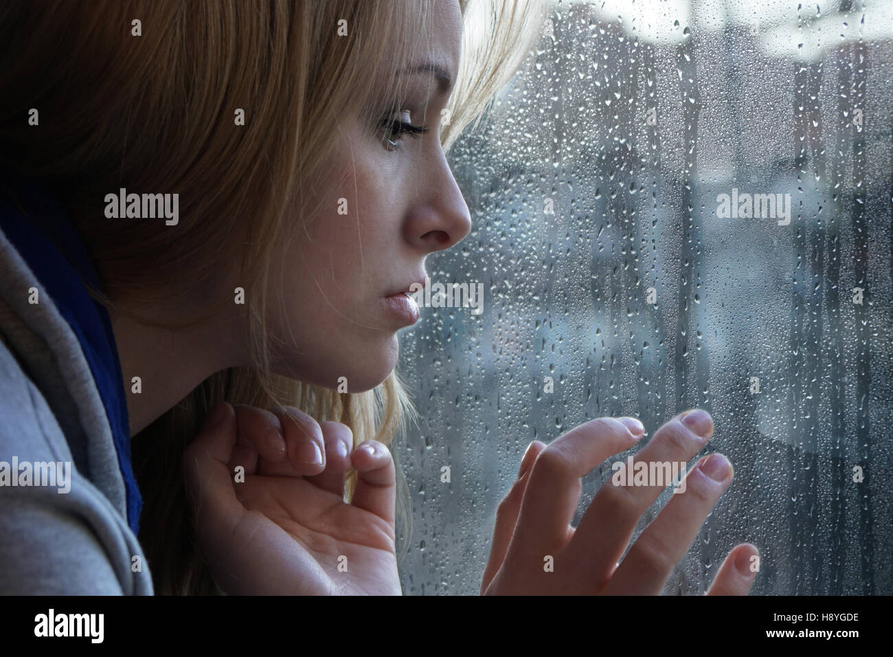 Triste giovane donna guardando attraverso la finestrella sul giorno di pioggia Foto Stock