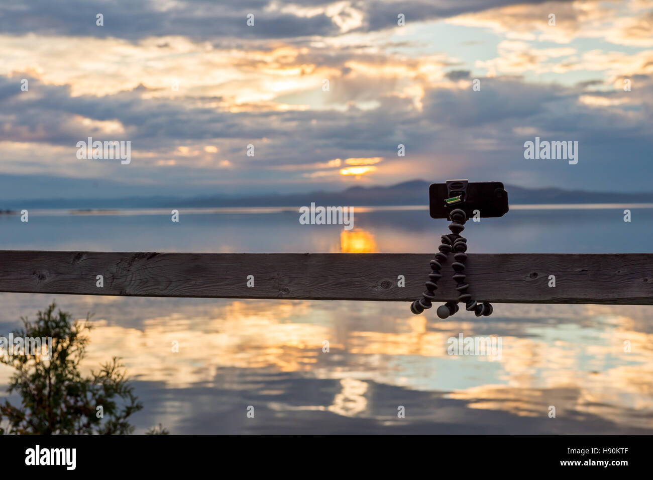 Smartphone collegato sul treppiede flessibile rivolto verso il mare al tramonto Foto Stock