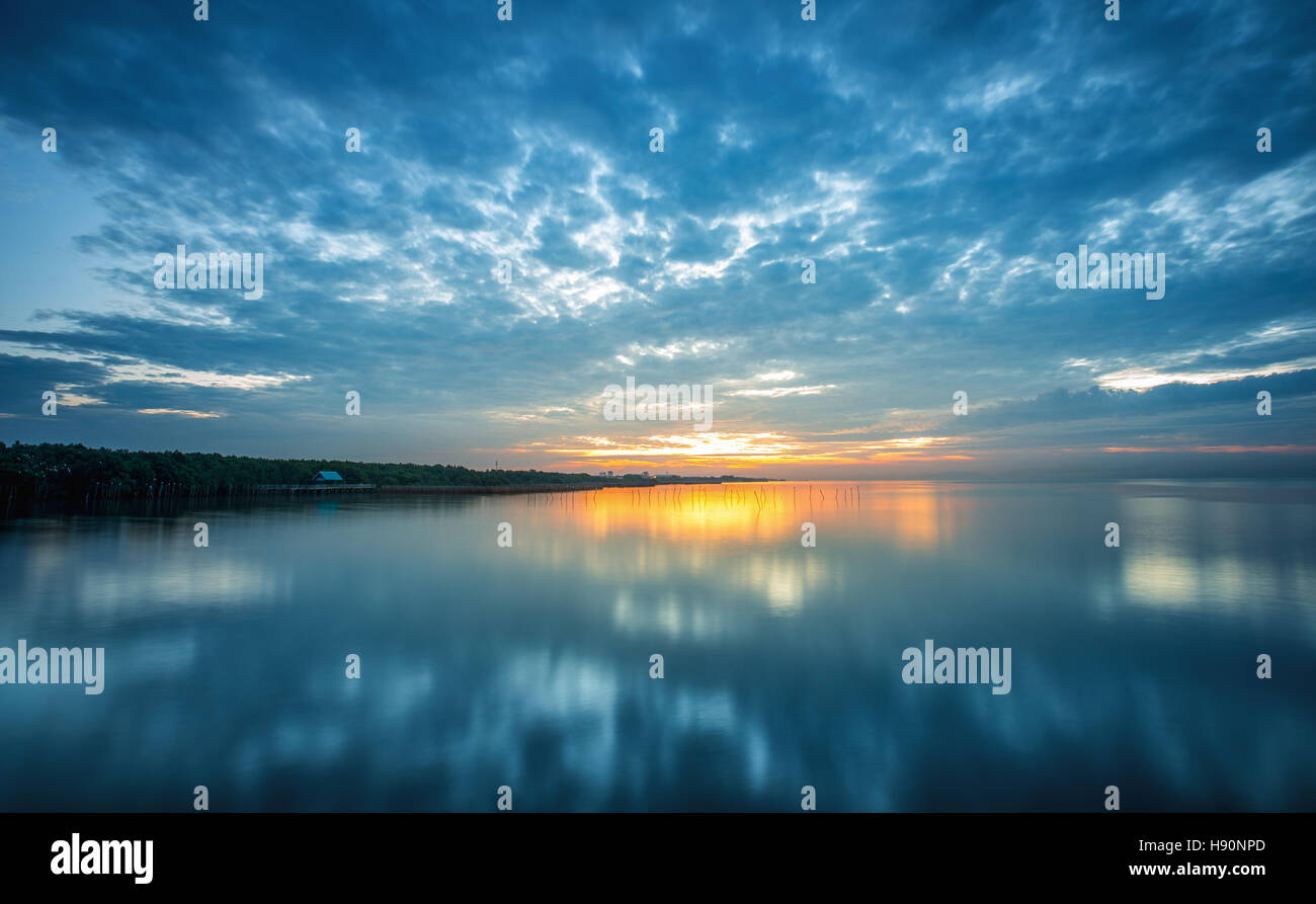 Panorama scena di blu cielo nuvoloso riflettendo su acqua piatta superficie con luce arancione prima di sunrise. Foto Stock