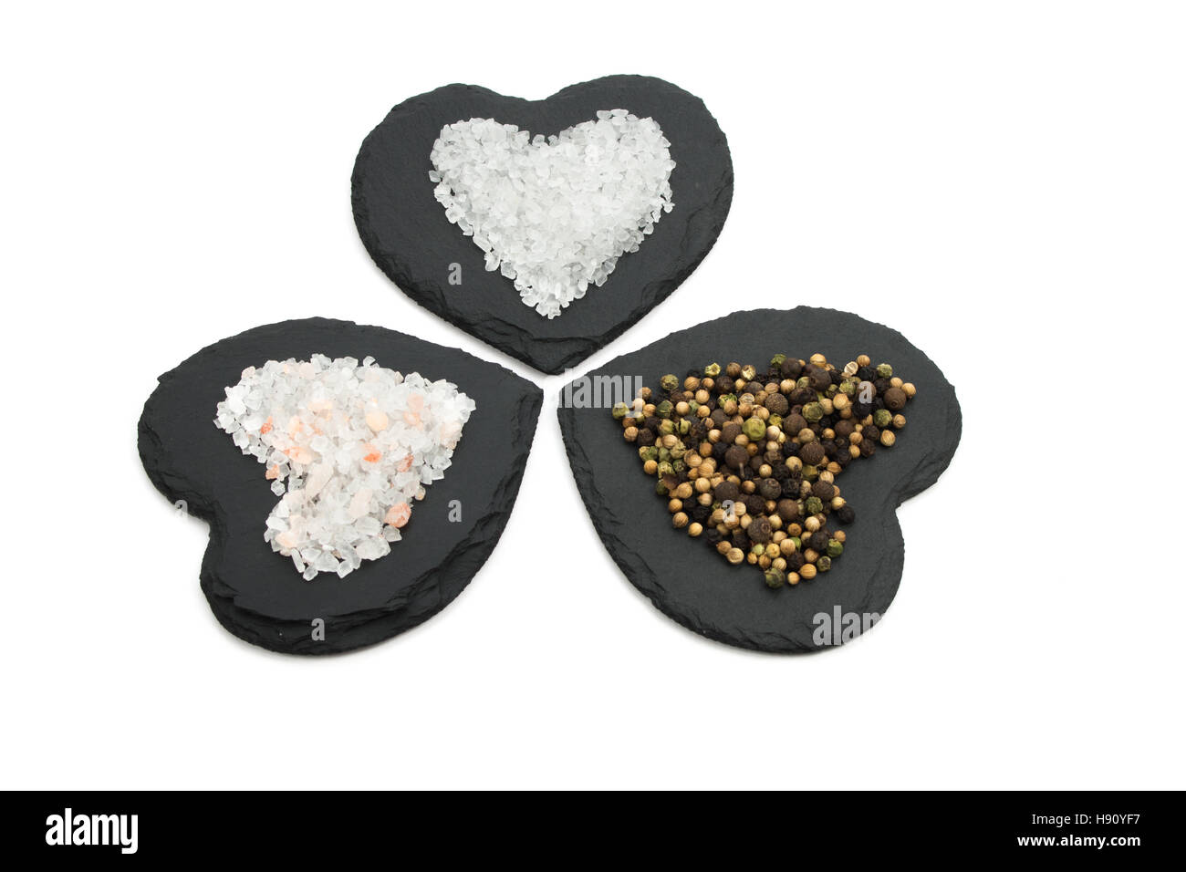 Il trio di grani di pepe e sali su a forma di cuore ad ardesie isolati su sfondo bianco Foto Stock