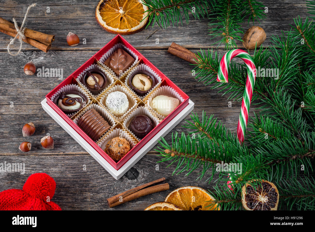 Regali di Natale, Natale decorazione: scatola di cioccolatini e caramelle, candy cane, spezie, frutta secca ed essiccata anelli arancioni sul tavolo di legno Foto Stock