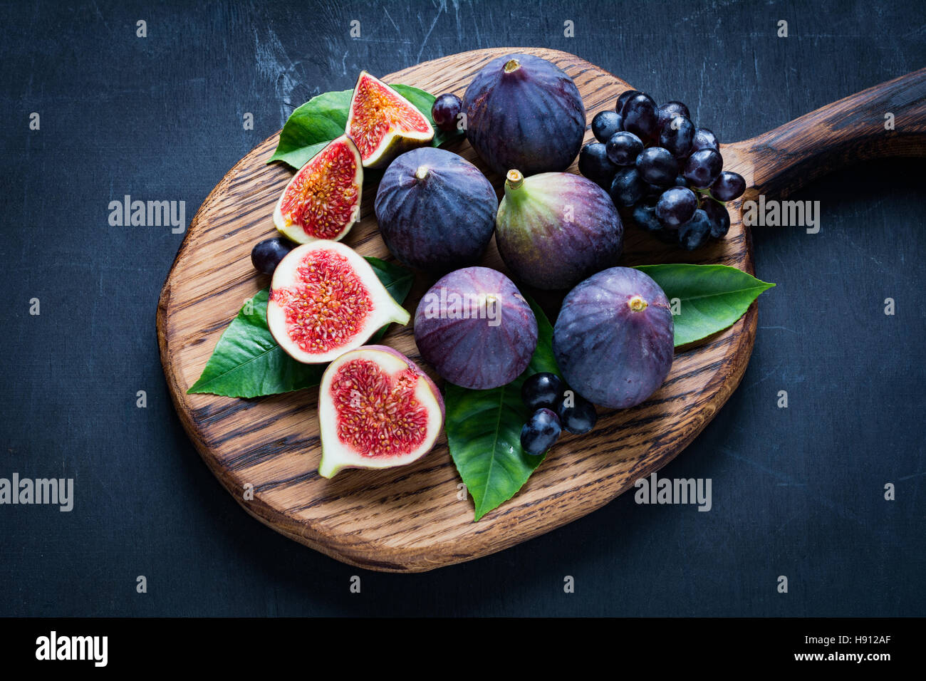 Un piatto di frutta fresca: fichi e uva nera "Isabella" sul tagliere di legno. Visualizzazione orizzontale Foto Stock