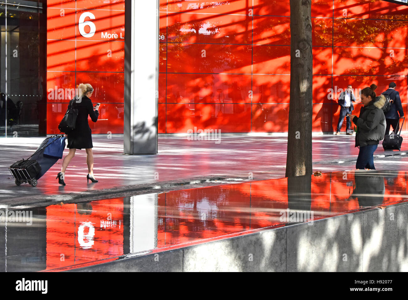 Fiducioso donna con carrello bagagli nella strada pedonale più in London Southwark England Regno Unito con il telefono cellulare, riflessi rosso in funzione dell'acqua Foto Stock