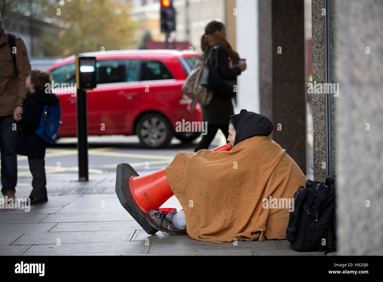 Senzatetto a mendicare per le strade di Londra che parla attraverso un cono stradale per i passanti su Victoria Street, Londra Centrale. Foto Stock