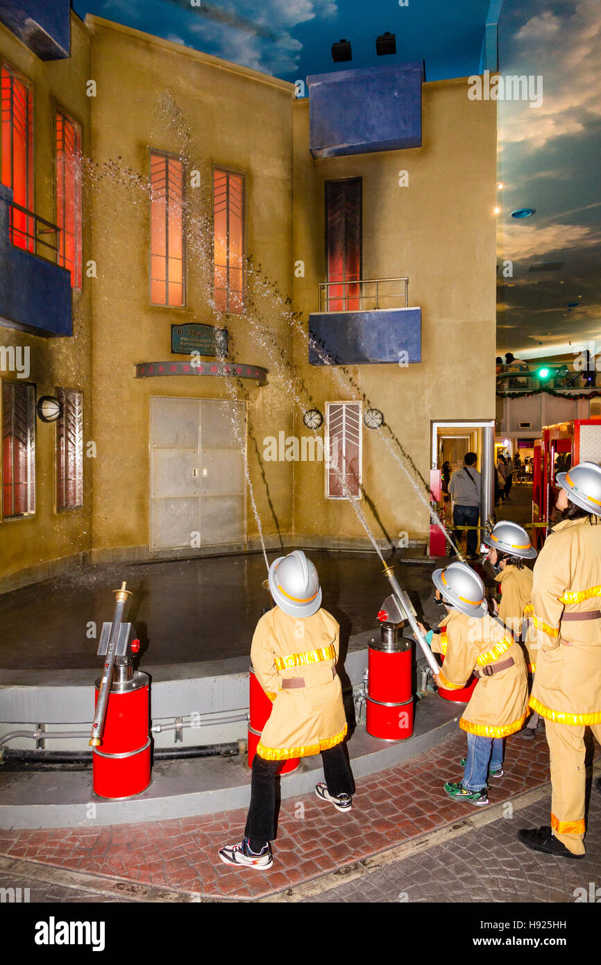 Giappone, Nishinomiya, KidZania, attività figlio il centro del gioco. Linea di bambini vestiti come i vigili del fuoco mirando tubi flessibili a combustione edificio. Foto Stock