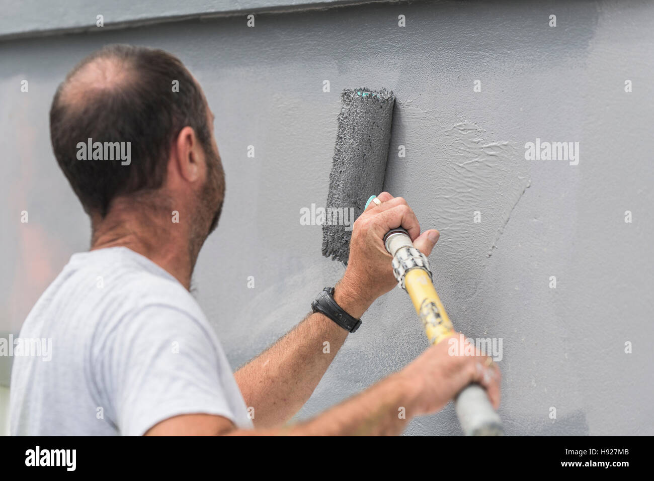 Un pittore e decoratore dipinge la parete esterna di una casa. Foto Stock