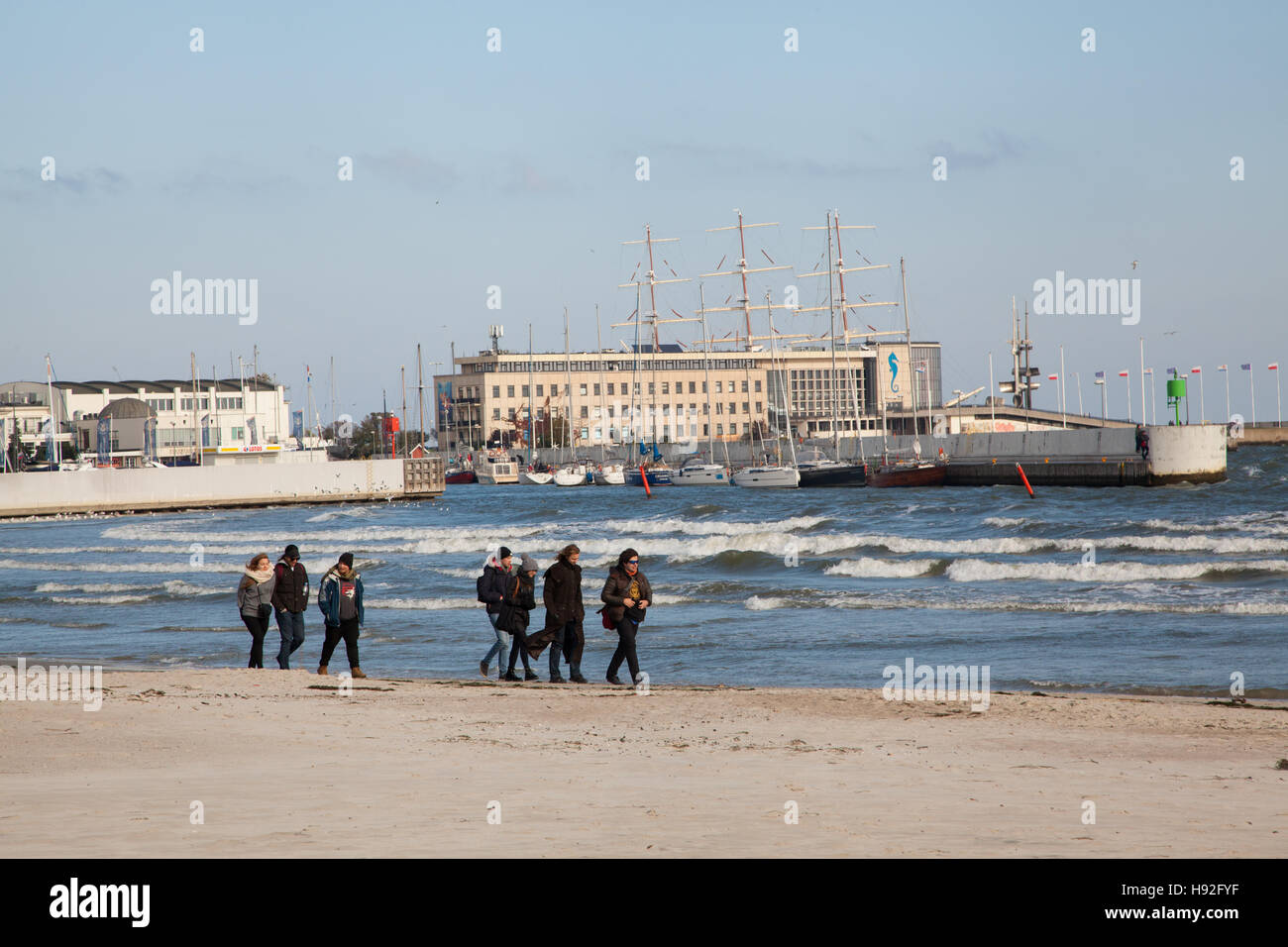 La gente camminare lungo la spiaggia a Gdynia sulla costa baltica della Polonia con il porto e la porta in background Foto Stock