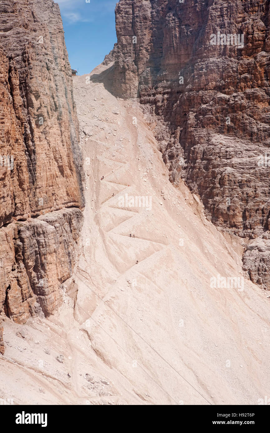 Walker scendendo un sentiero molto ripido, a zig-zag, scendendo dalla stazione sciistica di Canazei, Trentino, Alto Adige, Italia. Foto Stock