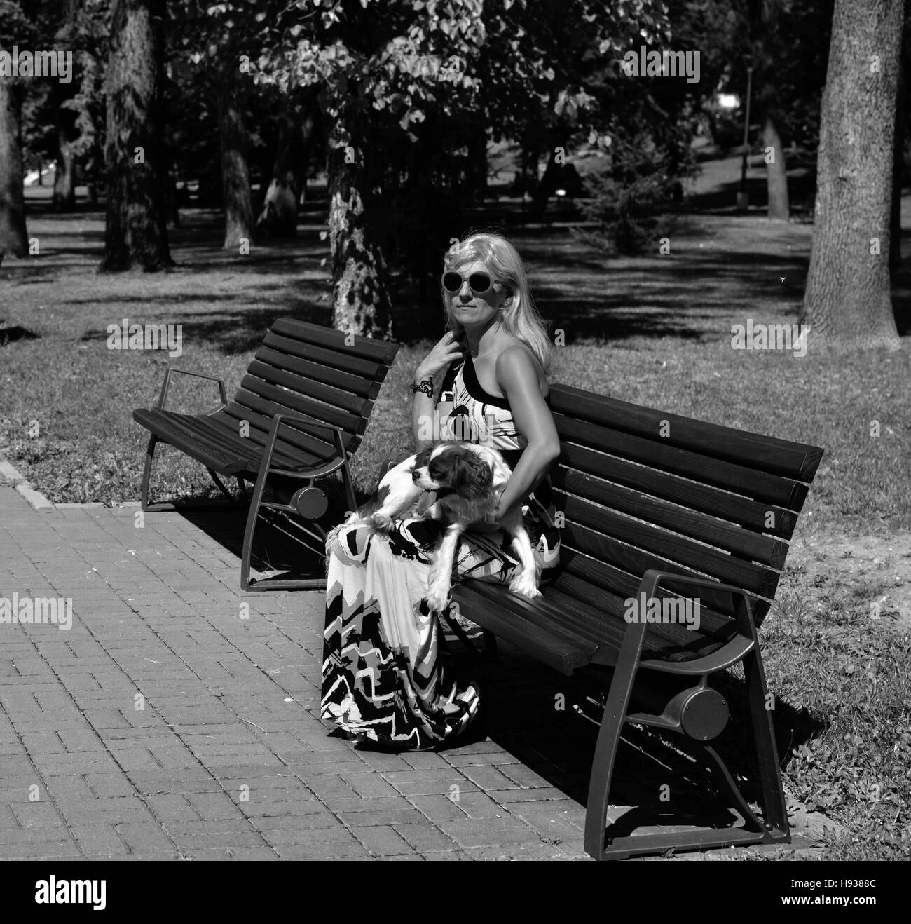 Immagine in scala di grigi di una donna che mantiene il suo cane e poggiante su una panchina nel parco pubblico Foto Stock