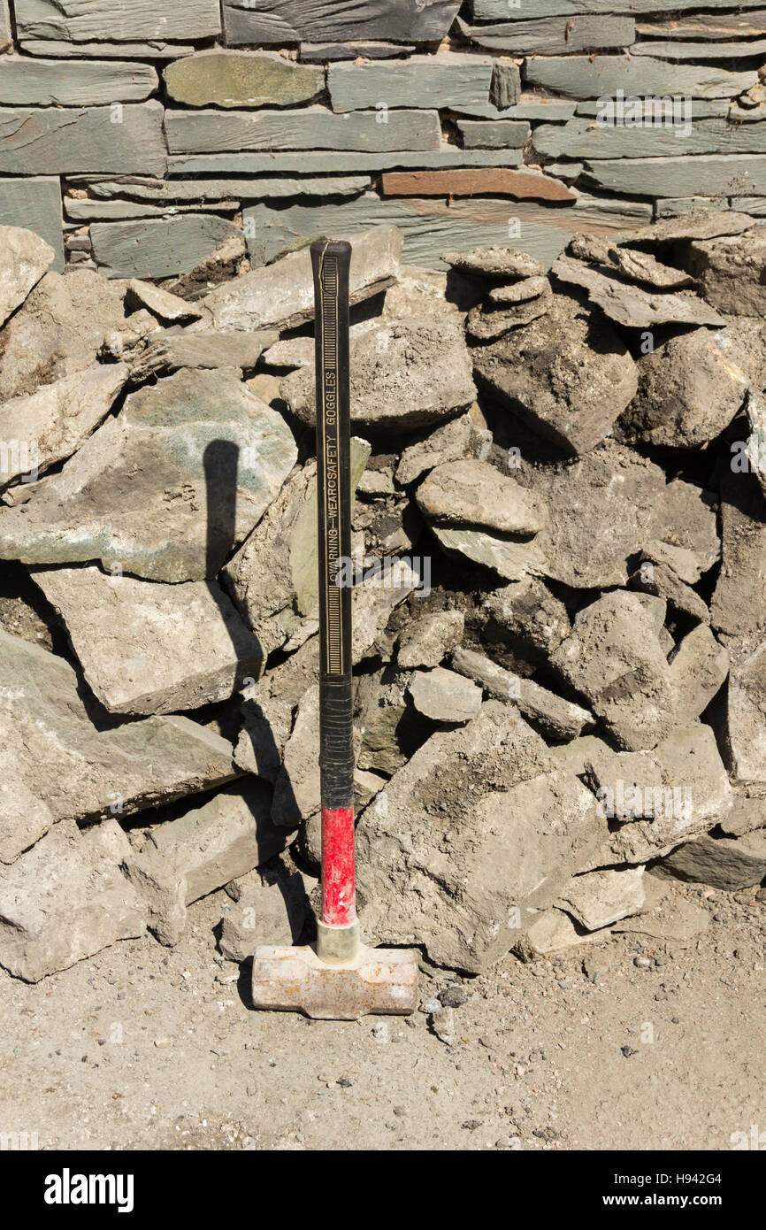 Mazza in piedi accanto a un mucchio di rotto rock accanto a un Lakeland parete ardesia. Parte di flood i lavori di riparazione che si svolgono in Glenridding, Cumbria. Foto Stock