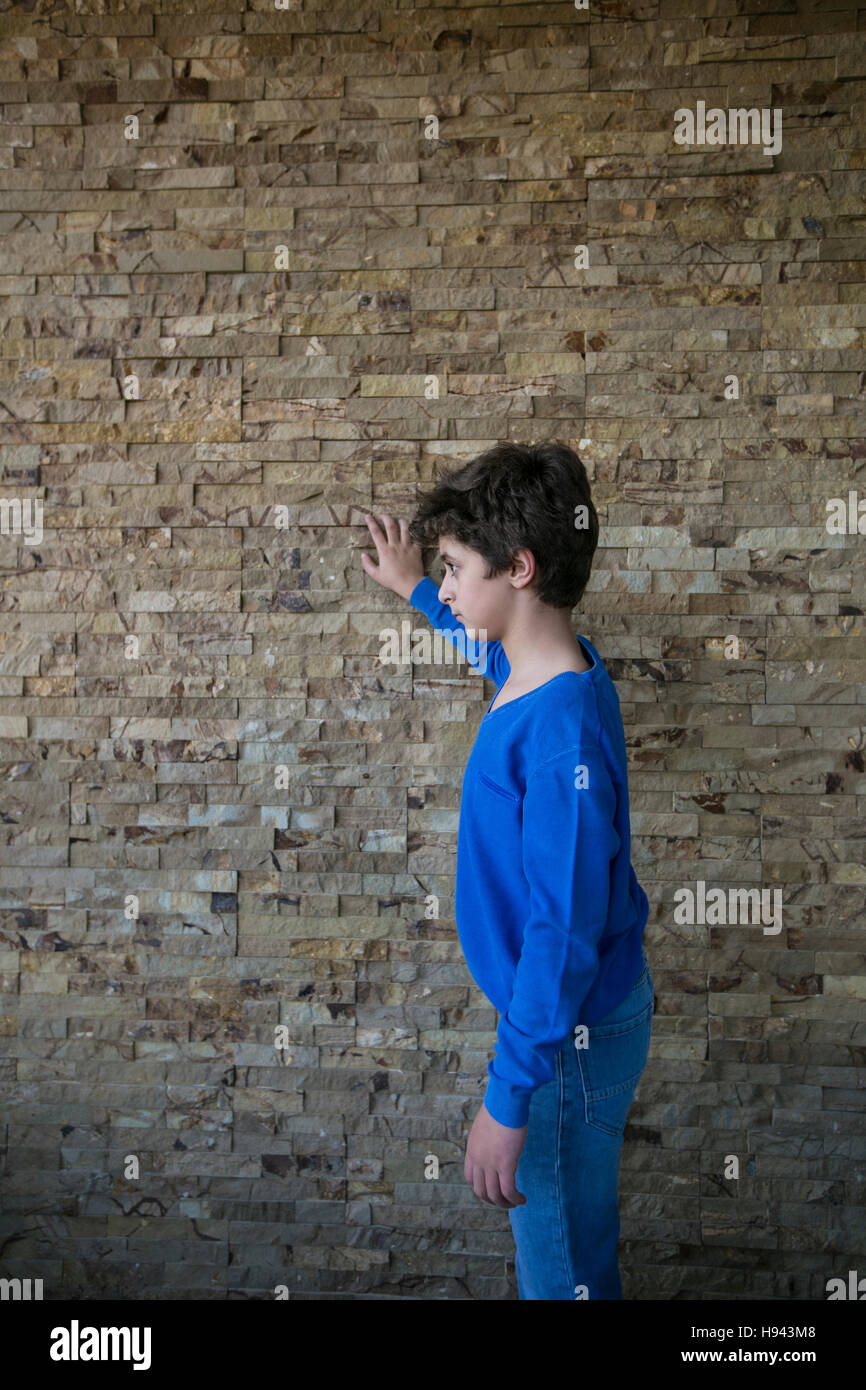Dieci anni vecchio ragazzo appoggiata contro il muro alla ricerca di distanza Foto Stock