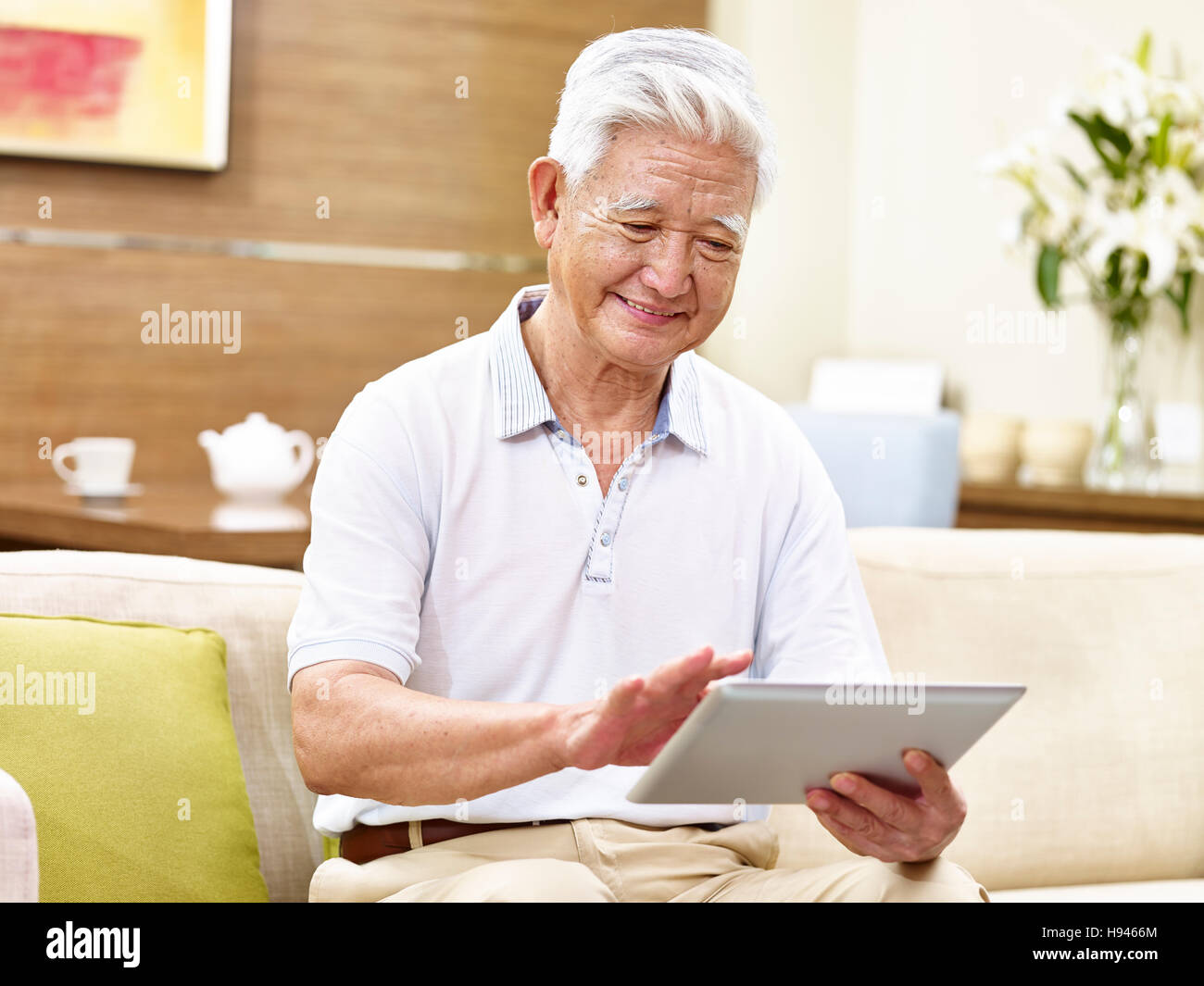 Active senior uomo asiatico seduto sul lettino usando computer tablet, rilassata, sorridente Foto Stock